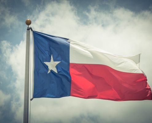 Large Texas (The Lone Star) flag waving on flag pole with cloud blue sky. Windy and sunny day with waving flag blowing/flowing. Ruffled Texas flag. Room for text, copy space. Vintage tone.