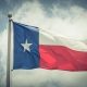 Large Texas (The Lone Star) flag waving on flag pole with cloud blue sky. Windy and sunny day with waving flag blowing/flowing. Ruffled Texas flag. Room for text, copy space. Vintage tone.